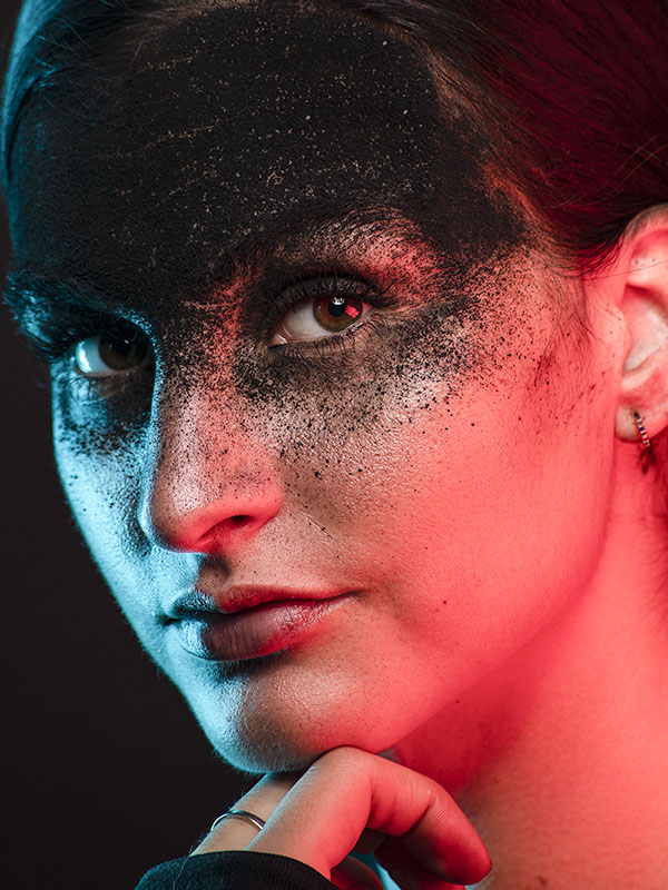 Lady with black powder covering top of her face, lit by color gels