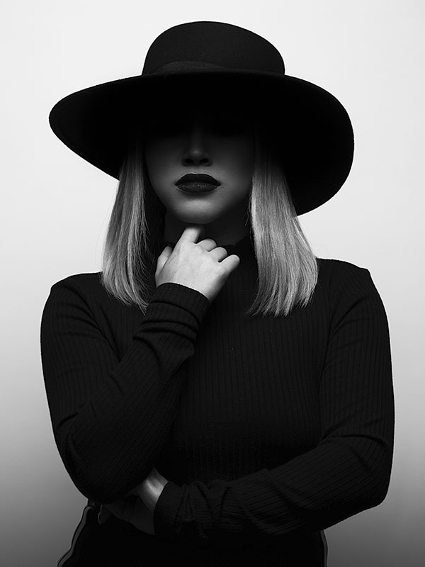 Black and white photo of a woman with crossed arms and a black hat covering the top of her face