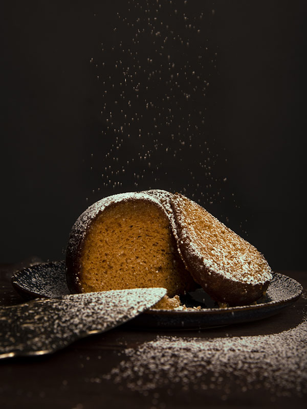 Freshly baked bunt cake sliced open on plate with powdered suger being sprinkled on top