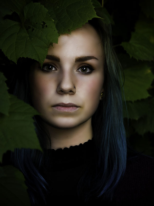 Woman with blue hair standing slightly behind green leaf