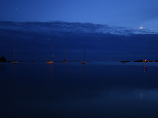 Grand Marais Harbor at night, sail boats in the distance, moon clouds star
